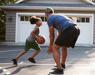 a dad and his daughter are playing basketball in the driveway of their home